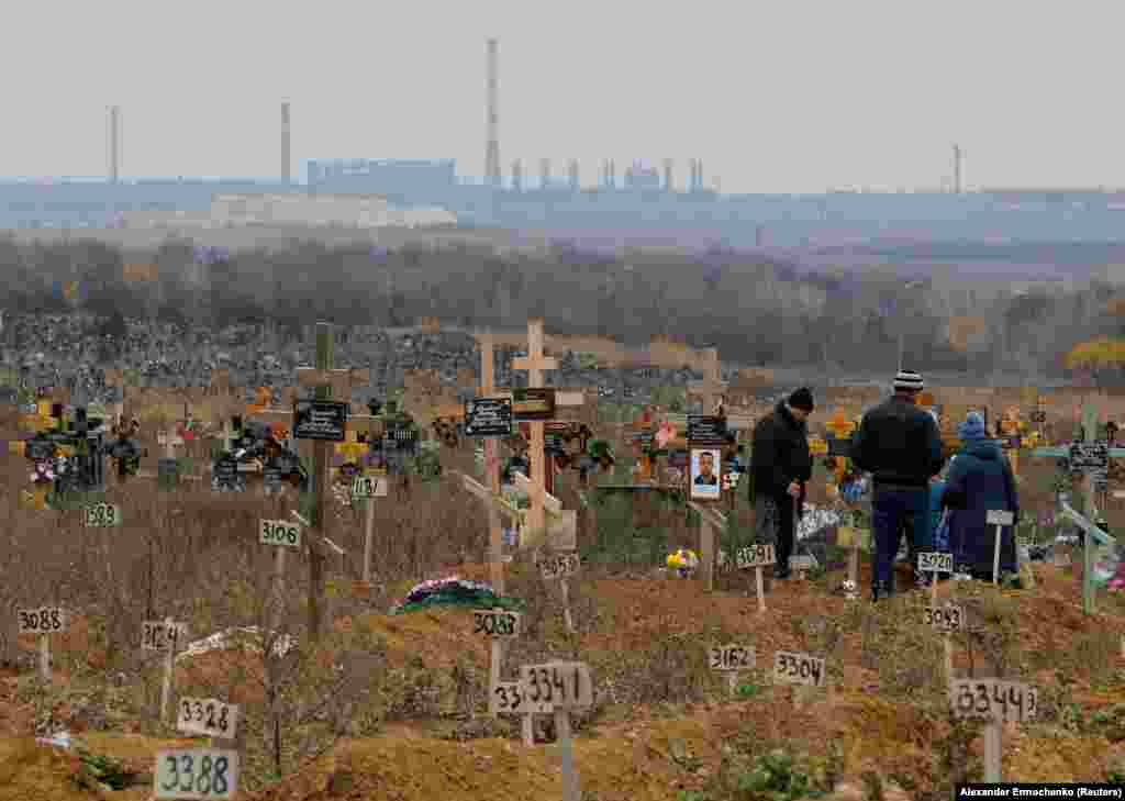 Люди відвідують могилу на Маріупольському кладовищі, 9 листопада 2022 року. Вважається, що десятки тисяч людей загинули під час майже тримісячної облоги Маріуполя російською армією, під час якої цивільні жили під майже постійними бомбардуваннями без світла та води, без доступу до медичної допомоги та продуктів харчування