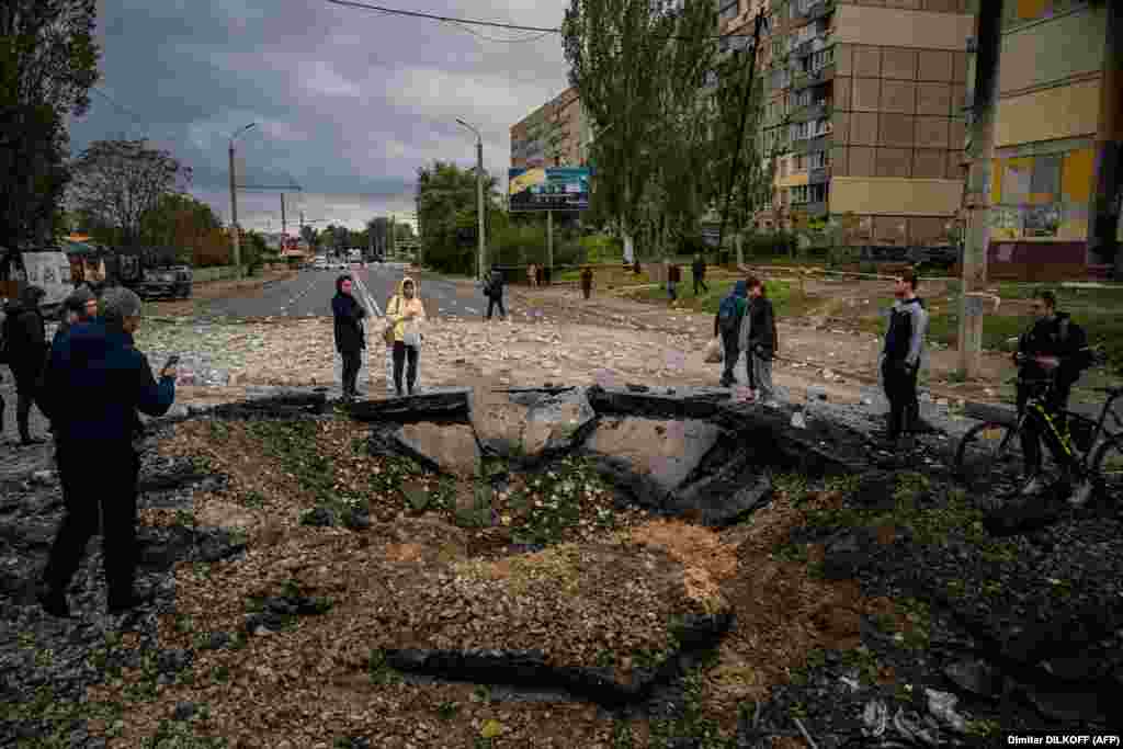 Люди дивляться на вирву, що утворилася внаслідок влучення російської ракети в одну із вулиць Дніпра. 10 жовтня 2022 року. Президент Росії Володимир Путін назвав ракетний терор проти українських міст &laquo;відплатою&raquo; за пошкодження Керченському мосту, що з&#39;єднує Росію з анексованим нею у 2014 році Кримом. Білий дім стверджує, що масована ракетна атака на міста України планувалася давно.