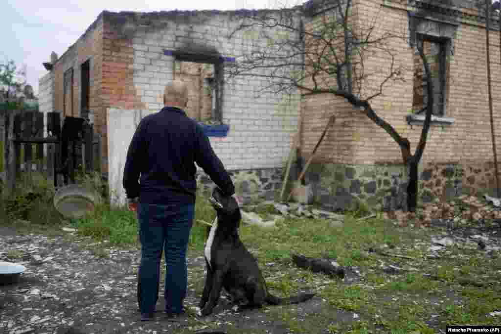 Едуард Зеленський гладить собаку і дивиться на те, що залишилося від його будинку після вторгнення Росії в Україну.