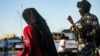 US-backed Syrian Democratic Forces (SDF) escort a fully veiled woman and a child in the northern Kuridish-Syrian city of Qamishli as Uzbek women and children linked to the Islamic State group are handed over to diplomats from the Central Asian country for